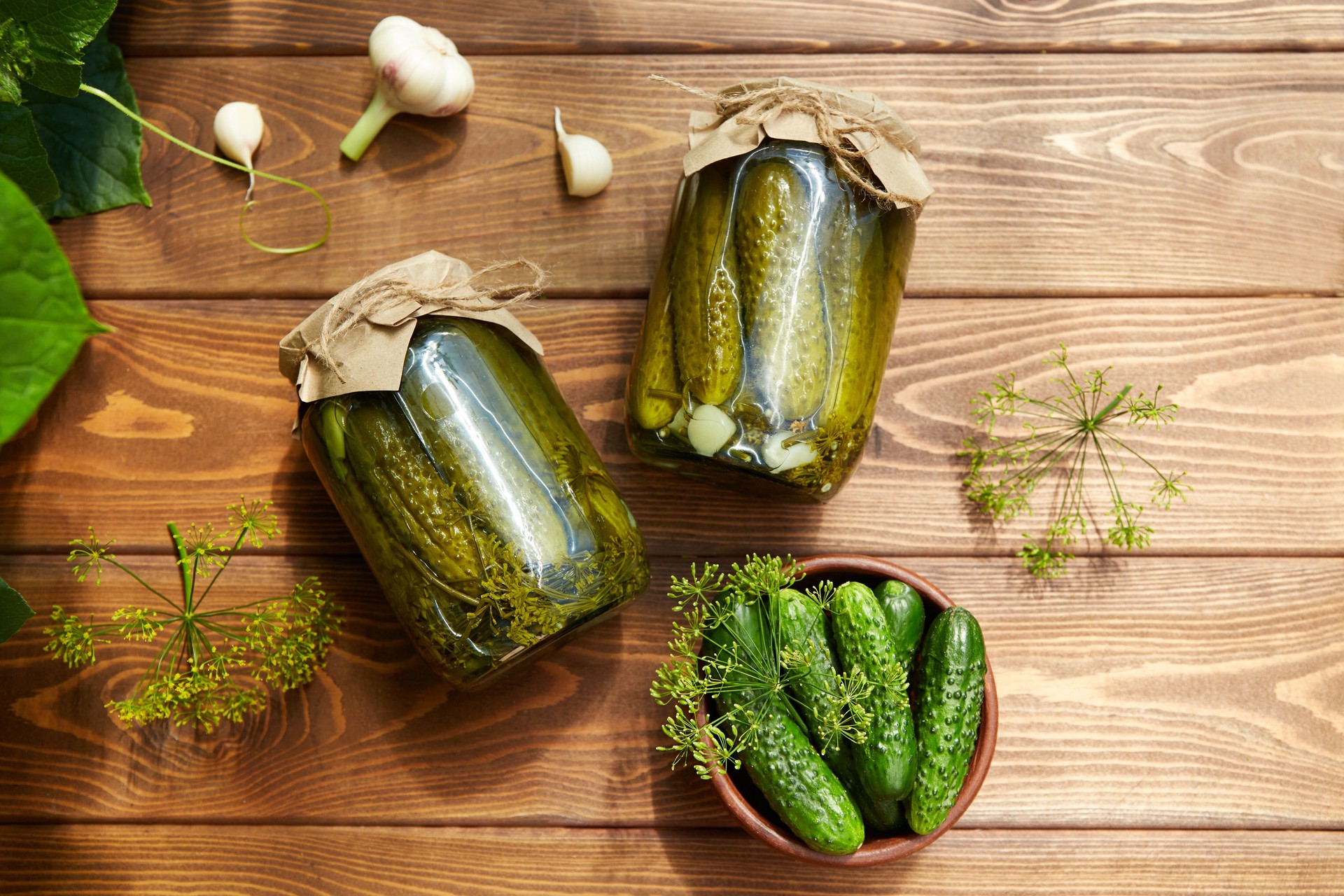 Pickled cucumbers in jars, fresh cucumbers on bowl, dill, garlic on a wooden background. Home canning.