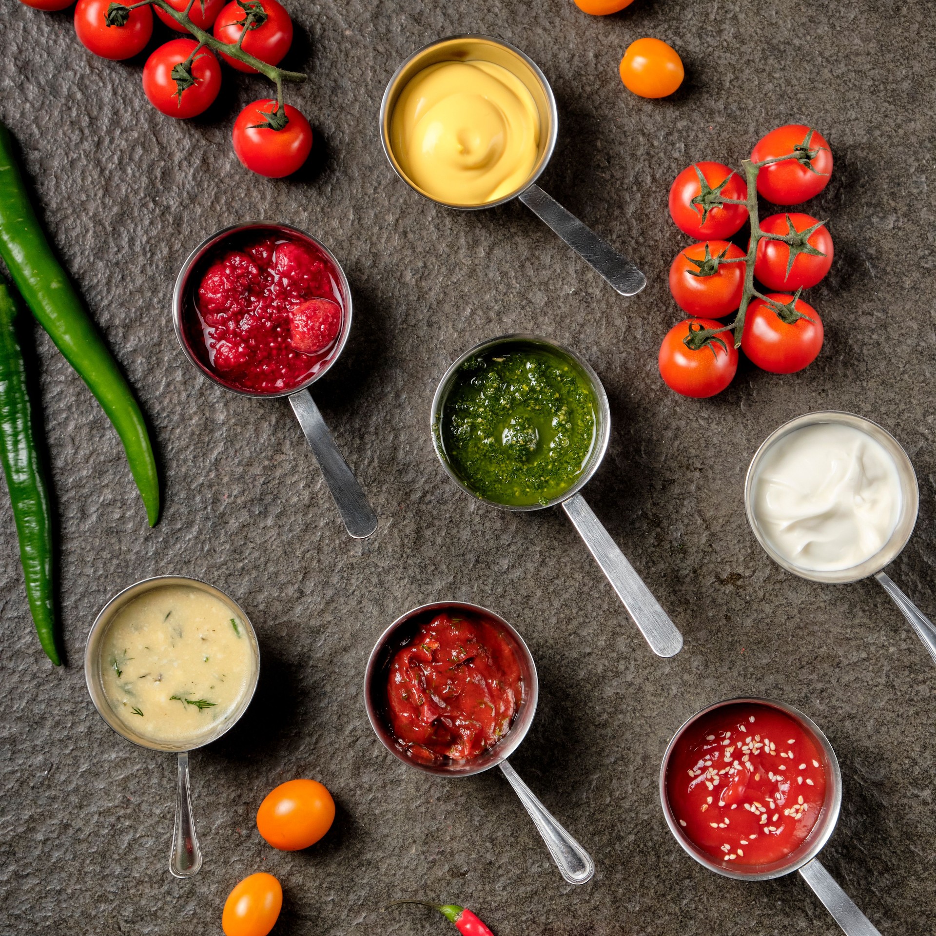 Set of different sauces - ketchup, mayonnaise, barbecue, mustard, grain hills, pesto, adzhika, chutney, tkemali sauce on on black stone background. Top view copy space